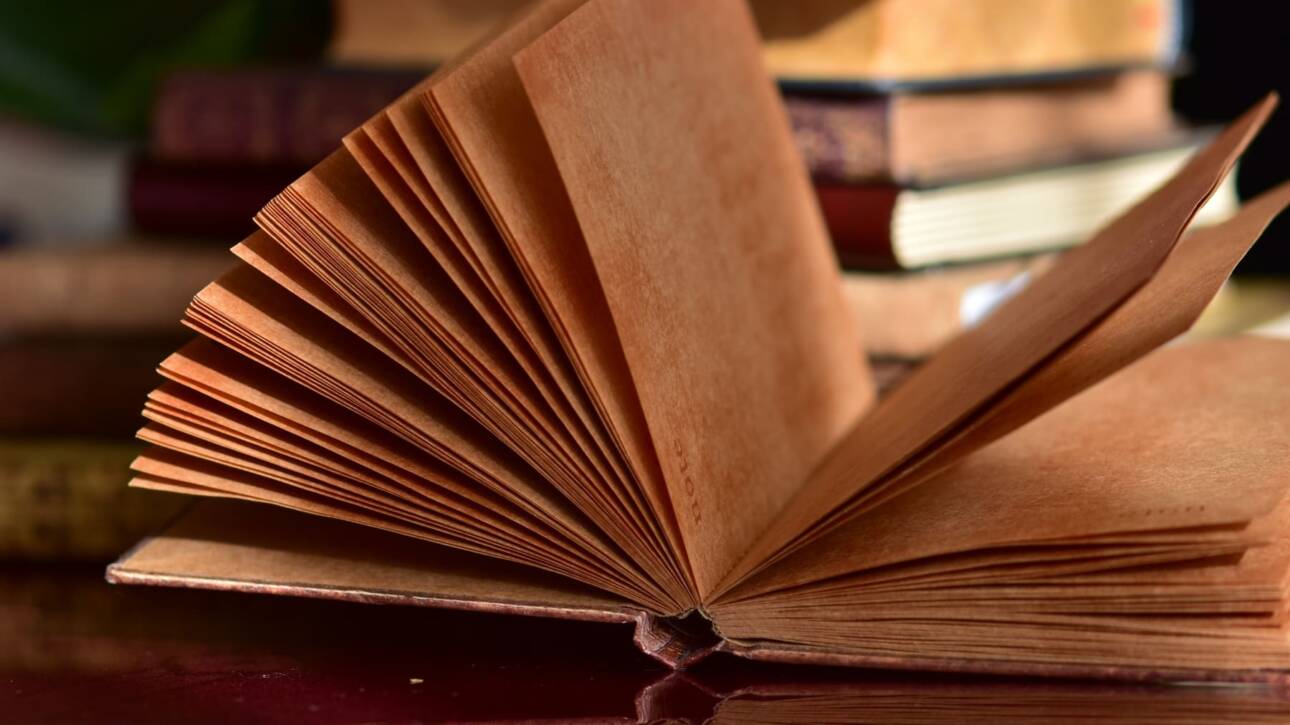 libro abierto frente a pila de libros en mesa de madera