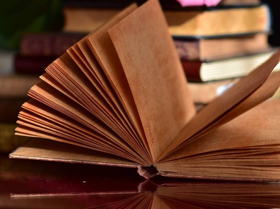 libro abierto frente a pila de libros en mesa de madera
