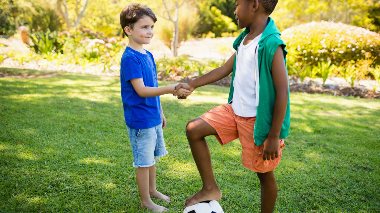 niños en cesped dandose la mano con balon de futbol