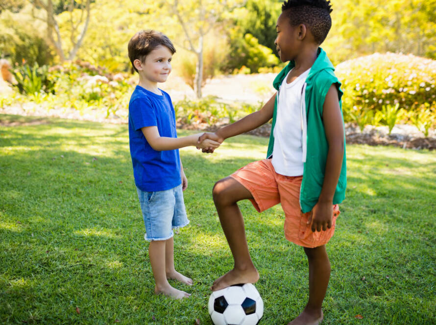 niños en cesped dandose la mano con balon de futbol