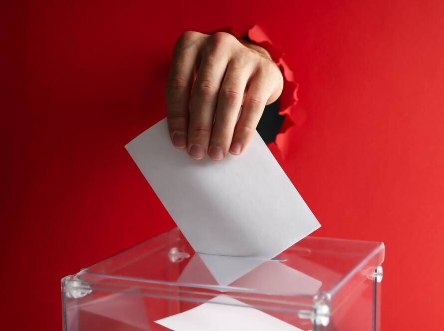 mano metiendo voto en urna con fondo rojo