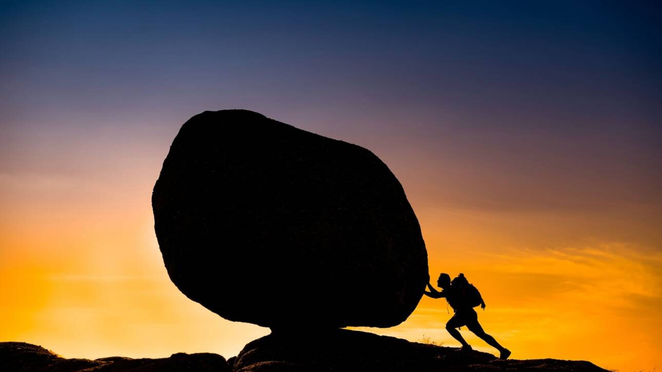 hombre empujando roca frente atardecer