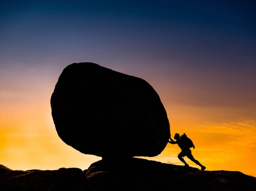 hombre empujando roca frente atardecer
